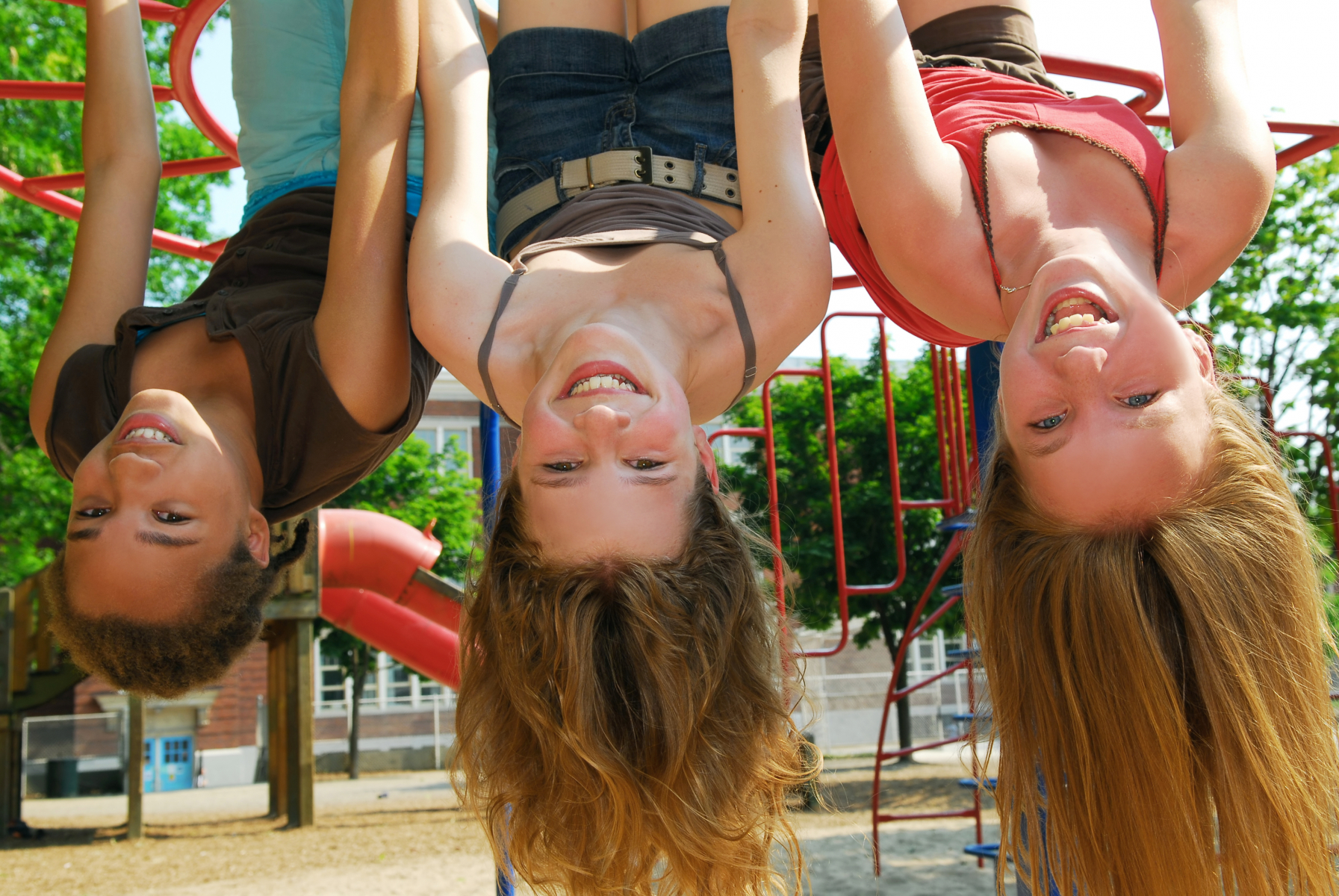 tre glada tjejer som hänger upp och ner i en lekpark