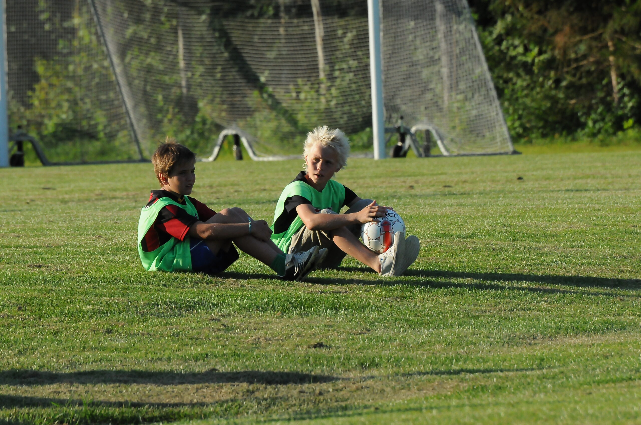 två småpojkar som sitter med en boll framför ett fotbollsmål utomhus