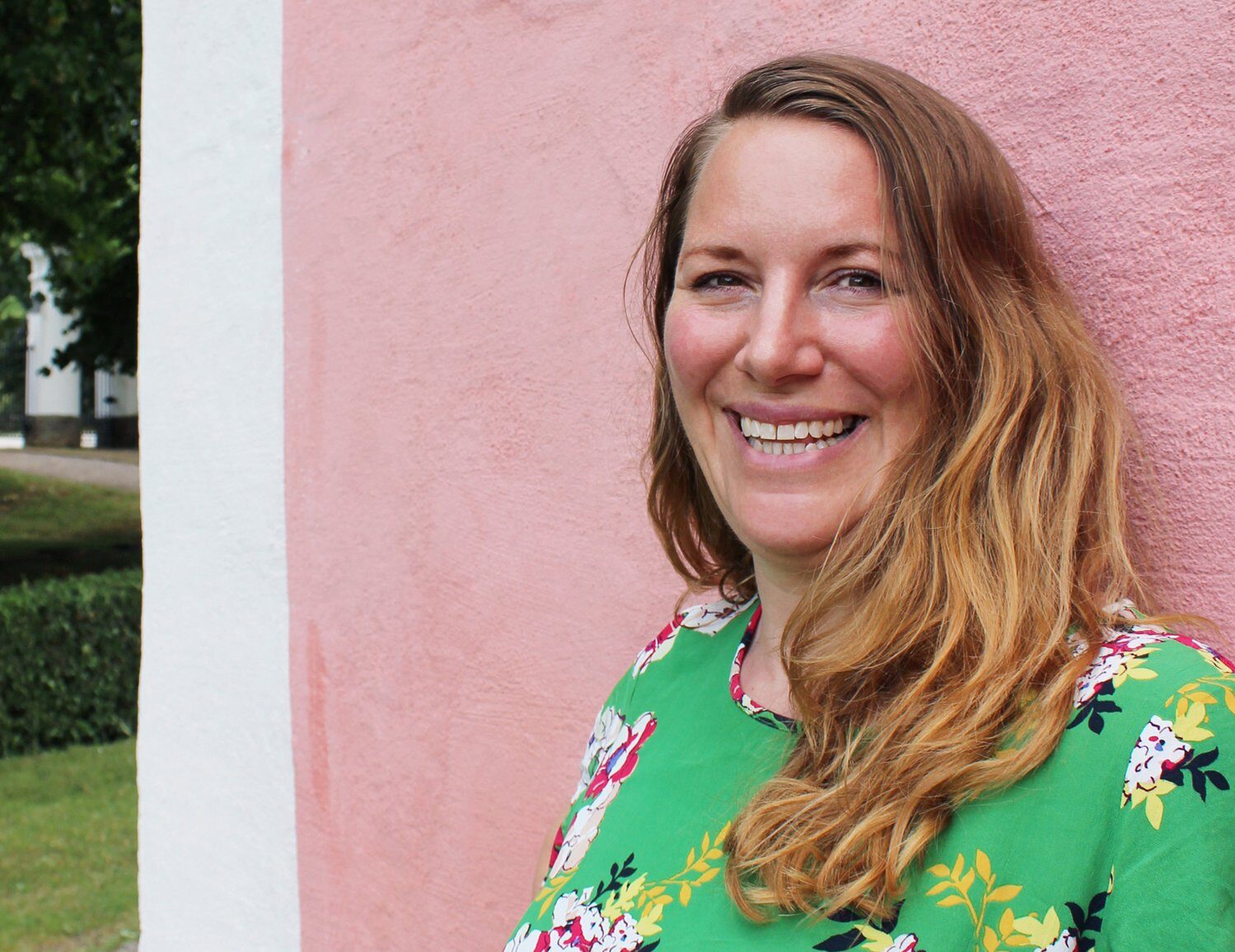 Sångerska Frida Knutsson i gröna kläder mot en rosa bakgrund'