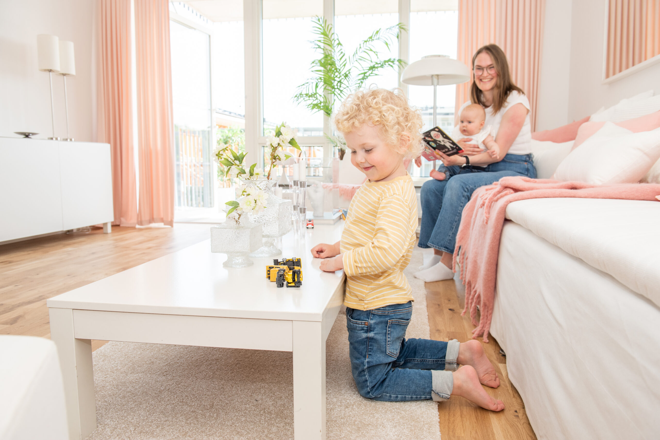 en mamma med två små barn som leker i ett vardagsrum i ljusa och rosa färger